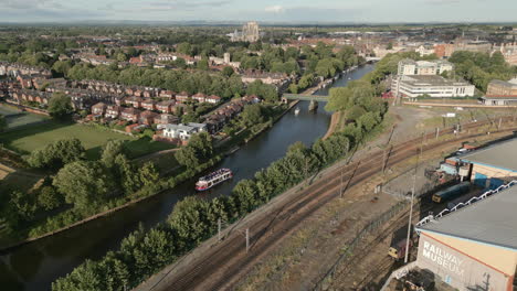 Pullback-Aerial-Drone-Shot-Revealing-National-Railway-Museum-with-York-Minster-Cathedral-and-River-Ouse-with-Tourist-Ferry-in-Background-on-Sunny-Evening-North-Yorkshire-UK