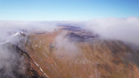 Drone-shot-pulling-backward-through-clouds-above-a-mountain,-Helvellyn,-Lake-District,-Cumbria,-UK