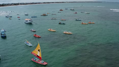 Dolly-out-aerial-drone-shot-of-the-Porto-de-Galinhas-or-Chicken-Port-beach-with-anchored-sailboats-and-tourists-swimming-in-the-crystal-clear-ocean-water-in-Pernambuco,-Brazil