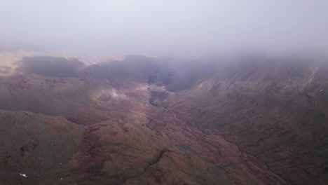 Drone-shot-flying-forward-through-through-mist-with-landscape-below,-Helvellyn,-Lake-District,-Cumbria,-UK