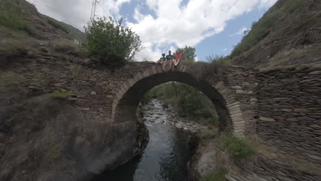 Sport-FPV-aerial-drone-flying-above-river-stream-towards-bridge-with-people