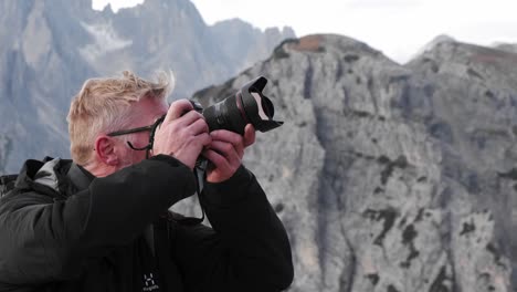 Hiker-Man-Taking-a-Photograph-with-a-Camera-on-Top-of-a-Mountain-in-Dolomites