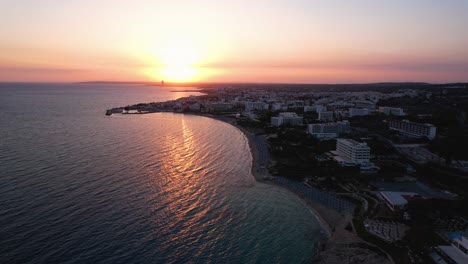 Magical-drone-shot-of-warm-golden-sunset-over-the-horizon-in-Ayia-Napa-Cyprus-with-reflection-on-calm-sea-water