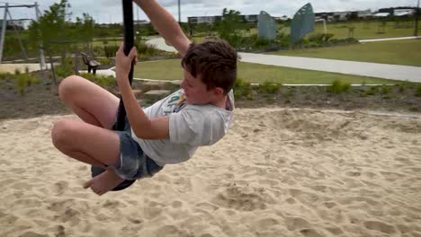 Excited-12-year-old-kid-spinning-around-on-a-swing-in-a-public-park