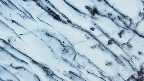 Tourist-group-exploring-cracked-surface-of-ice-glacier-in-Iceland,-top-down