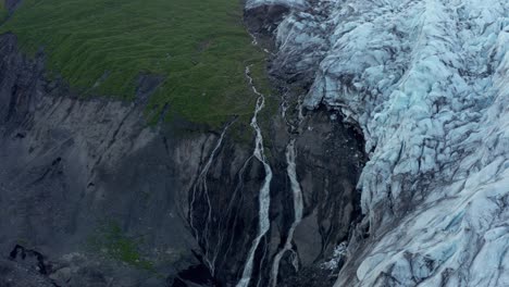 Melt-water-from-glacier-flowing-from-mountain-cliff,-aerial