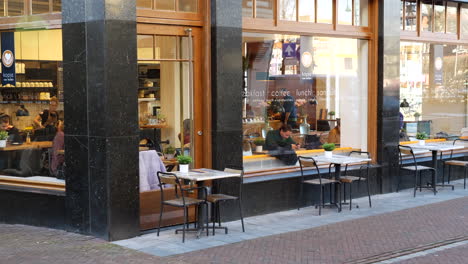 Static-shot-of-people-sitting-in-modern-dutch-cafe-and-working-during-sunny-day-outdoors---slow-motion