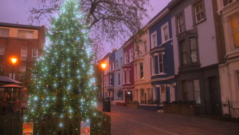 Tilt-down-shot-of-beautifully-decorated-Christmas-tree-in-Notting-Hill,-London,-UK-surrounded-by-residential-houses-during-evening-time