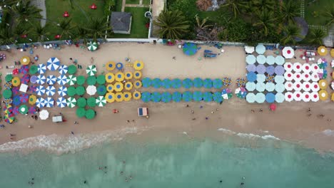 Bird's-eye-top-down-aerial-drone-shot-of-colorful-umbrellas,-food-vendors,-and-tourists-swimming-in-the-natural-pools-in-the-famous-Porto-de-Galinhas-or-Chicken-Port-beach-in-Pernambuco,-Brazil