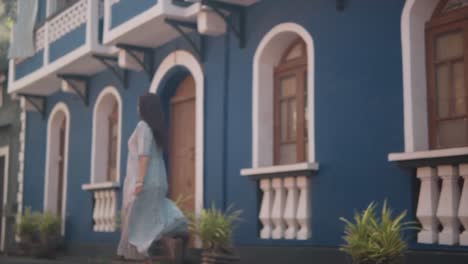 Morena-Mujer-India-Felizmente-Caminando-Y-Dando-Vueltas,-Frente-A-Un-Edificio-Azul-En-Las-Calles-Históricas-De-Fontainhas,-India