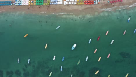 Bird's-eye-top-down-aerial-shot-of-the-famous-Porto-de-Galinhas-or-Chicken-Port-beach-in-Pernambuco,-Brazil-with-colorful-umbrellas,-tourists-swimming-in-the-natural-pools,-and-anchored-sailboats