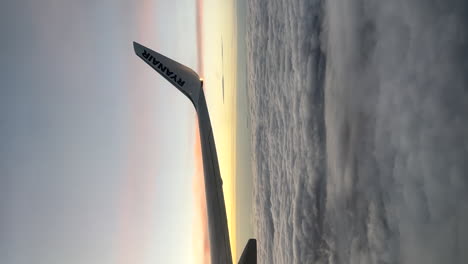 Vertikaler-Ryanair-flugzeugflügelblick-Vom-Passagierfenster-über-Den-Glühenden-Sonnenuntergangswolkenhorizont
