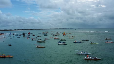 Trucking-right-aerial-drone-shot-of-the-famous-Porto-de-Galinhas-or-Chicken-Port-beach-with-dozens-of-anchored-sailboats-and-tourists-swimming-in-the-crystal-clear-ocean-water-in-Pernambuco,-Brazil