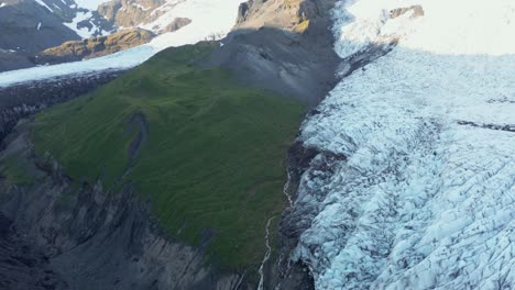 Iceland-natural-landscape-with-green-grass-mountain-slope-with-ice-glacier,-aerial