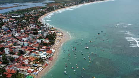 Rising-tilting-up-aerial-drone-wide-shot-of-the-Porto-de-Galinhas-or-Chicken-Port-beach-with-anchored-sailboats-and-tourists-swimming-in-the-crystal-clear-ocean-water-in-Pernambuco,-Brazil