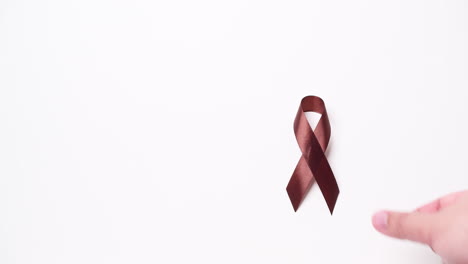 Detail-of-male-hand-holding-ribbon-in-brown-color-over-white-background
