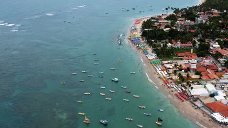Tilting-up-aerial-drone-wide-shot-of-the-Porto-de-Galinhas-or-Chicken-Port-beach-with-anchored-sailboats-and-tourists-swimming-in-the-crystal-clear-ocean-water-in-Pernambuco,-Brazil