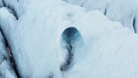 Ice-cave-in-white-frozen-glacier-in-Iceland,-erosion-from-water,-aerial