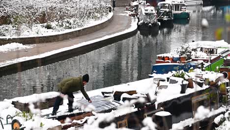 Clearing-the-rooftop-of-a-Canal-Boat-after-some-snow,-Regents-Canal,-London,-United-Kingdom