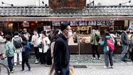 People-with-face-masks-on-crowded-food-market-street-in-Nara,-Japan