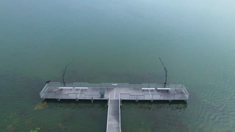 Flyover-of-fishing-dock-and-aerial-reveal-of-Starke-Lake-and-cloudy-sky-in-Ocoee,-Central-Florida
