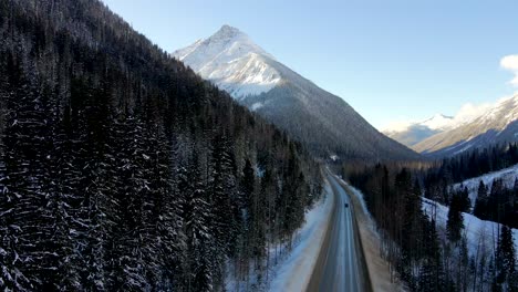 Trans-Canada-Highway-1-Winter-Journey:-a-black-car-travels-Across-Scenic-Landscape-with-Majestic-Mountains-and-snow-covered-forests-in-Revelstoke,-British-Columbia