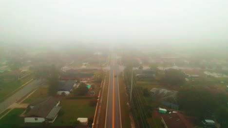 Aerial-reverse-flyover-of-foggy-and-misty-road-through-city-of-Ocoee,-Florida-with-solo-vehicle-driving