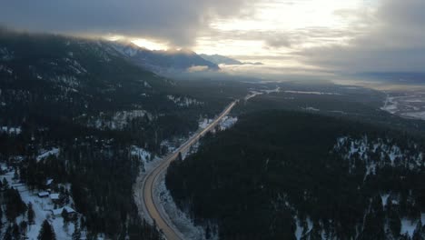 Panoramic-View-of-Cariboo-Highway-95-Running-into-the-Horizon-Surrounded-by-Impressive-Mountains-Range-Covered-in-Clouds-During-Sunrise-Warm-Light:-warm-light-,-spectacular-aerial-approach-shot