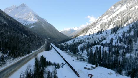 Freight-Train-Traveling-through-Snowy-Forests-and-Majestic-Mountains-in-Revelstoke,-British-Columbia:-Winter-Wonderland-from-Above
