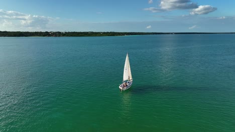 Lonely-sailboat-sailing-on-the-laguna-Bacalar,-in-sunny-Quintana-Roo,-Mexico---Aerial-view