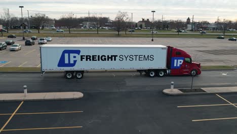 drone-tracking-shot-of-a-red-semi-truck-with-white-trailer-driving-in-a-parking-lot-on-a-busy-day