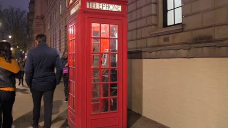Gente-Caminando-En-La-Calle-Con-Cabina-Telefónica-Roja-Por-La-Noche-En-Londres,-Reino-Unido