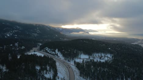 Sonnenaufgang-Warmes-Licht-Beleuchtet-Cariboo-Highway-95,-Umgeben-Von-Majestätischen,-Wolkenbedeckten-Bergen:-Atemberaubende-Luftaufnahme-Mit-Panoramablick