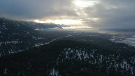 Aerial-View-of-Cariboo-Highway-95-Running-into-the-Horizon-Surrounded-by-Impressive-Snow-Covered-Mountains-and-Forests-During-Warm-Sunrise:-Panoramic-Scene-of-Spectacular-Winter-Landscape