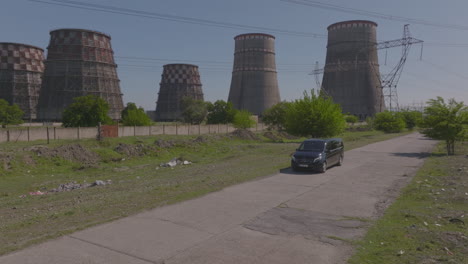 tracking-shot-of-a-suv-starting-to-drive-away-from-a-power-station-with-chimney-stacks