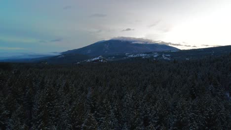Drohnenperspektive:-Rückwärtsflug-über-Eine-Schneebedeckte-Wald--Und-Berglandschaft-In-Einem-Warm-Beleuchteten-Himmel-In-British-Columbia,-Kanada