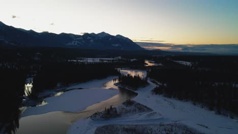 Aerial-Approach-Shot-of-Beautiful-Winter-Landscape-During-Golden-Hour,-Showing-River-with-Reflection-and-Majestic-Mountains-in-the-Distance-in-British-Columbia,-Canada