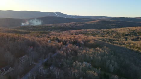 An-aerial-shot-in-New-England-specifically-Vermont-showing-the-ski-mountains-in-the-background-and-a-cloud-of-smoke-in-the-distance