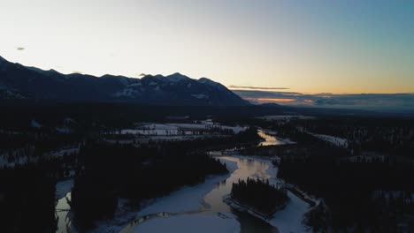 Aerial-Unveiling-of-Gorgeous-Winter-Landscape-During-Golden-Hour:-Bird's-Eye-View-of-Reflective-River-and-Stately-Mountains-in-British-Columbia,-Canada