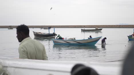 Dolly-Left-Reveal-Of-Small-Boats-Floating-In-Harbour-Waters-In-Gwadar-On-Coast-Of-Balochistan-With-Local-Fisherman-Walking-Past