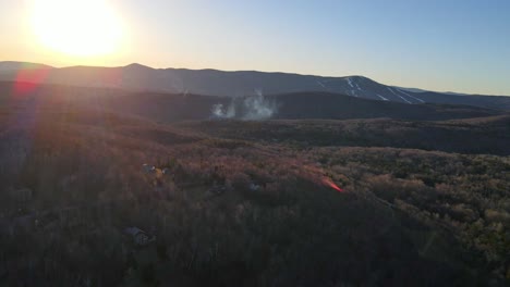 A-drone-shot-in-New-England-specifically-Vermont-showing-the-ski-mountains-in-the-background-and-a-cloud-of-smoke-in-the-distance