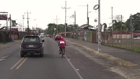 Man-riding-bicycle-overtaken-by-SUV-car-in-a-low-income-area-of-the-city,-Slow-motion-follow-behind-shot