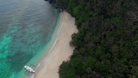 Drone-shot-of-a-lone-boat-anchored-along-white-sand-beach-in-an-isolated-island