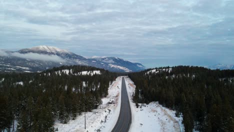 Cloudy-Blue-Hour-Aerial-View-of-Cariboo-Highway-95-Running-into-the-Horizon-Surrounded-by-Impressive-Snow-Covered-Mountains-and-Forests:-Panoramic-Scene