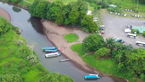 Tarcoles-river-with-tour-boats-in-Costa-Rica-with-bus-transportation-nearby,-Aerial-pan-right-shot