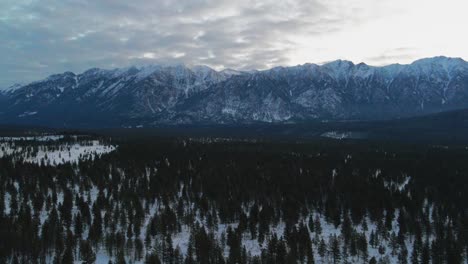 Toma-Aérea-Lateral-De-Impresionantes-Montañas-Y-Bosques-Cubiertos-De-Nieve-En-Un-Día-Nublado-Durante-El-Amanecer-En-Columbia-Británica,-Canadá:-Impresionante-Paisaje-Invernal