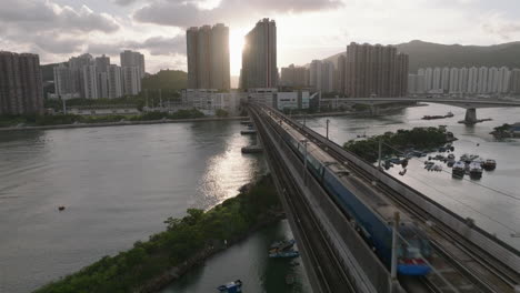 Pull-away-aerial-shot-of-train-passing-over-bridge-from-Tsing-Yi-Island-to-Ma-Wan,-Hong-Kong,-with-sun-flares-in-the-background