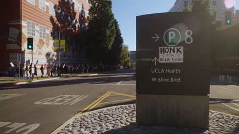 A-Sign-that-Says-"Honk-for-Academic-Workers,"-with-a-Picket-Line-Marching-in-the-Background-at-UCLA