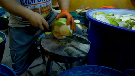 Man-peeling-coconut-using-sharp-knife-and-placing-them-into-water-in-large-bin