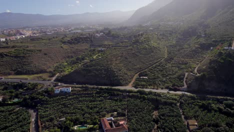 Aerial-View-Of-Plantations-On-Hillside-Near-Local-Town-In-Tenerife-With-Highway-Running-Through-It